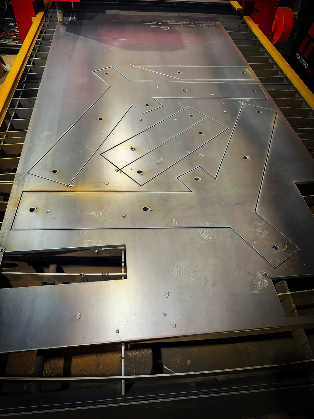 CNC plasma-cut steel plate on the cutting bed, cut lines and holes visible